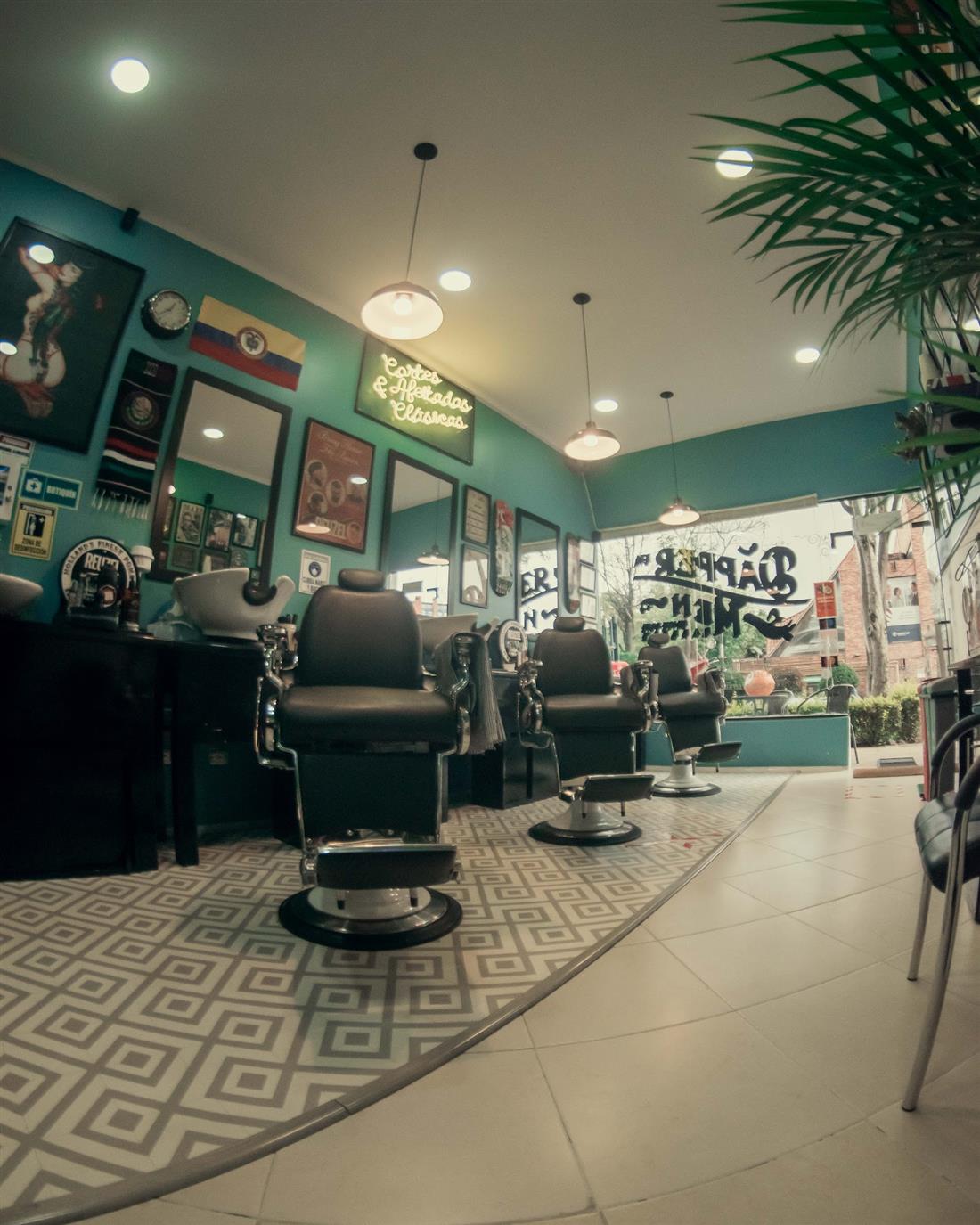 Interior de Dapper Men con muro verde azulado, sillas de barbero clásicas y neón 'Cortes & afeitados clásicos'