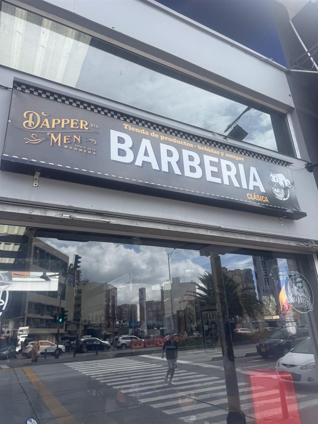 Letrero 'Barbería' de Dapper Men sobre la vitrina, con la calle reflejada