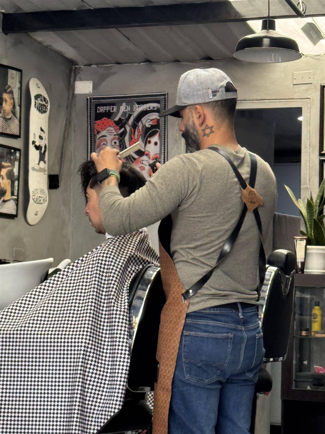Barbero de Dapper Men cortando con tijera y peine a un cliente con capa de cuadros
